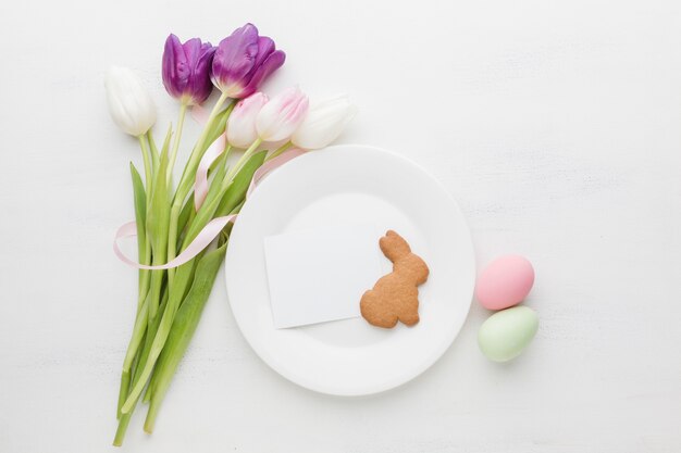 Flat lay of bouquet of tulips with plate and colorful easter eggs