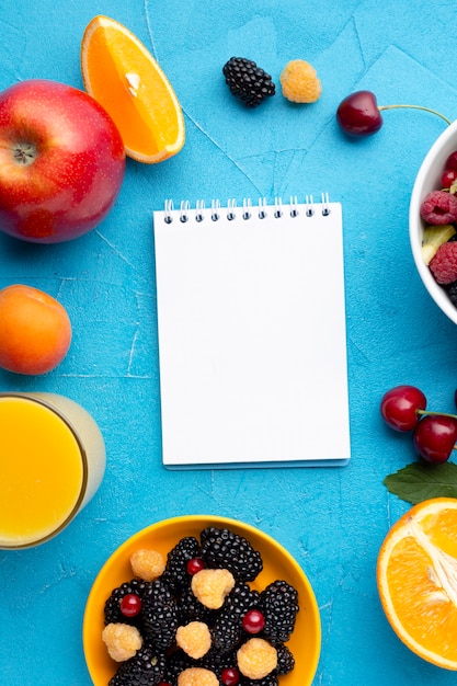 Free photo flat-lay bowl of fresh berries and fruits with notepad