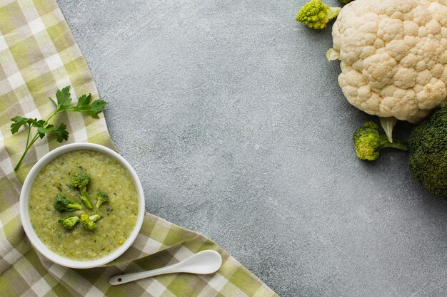 Flat lay broccoli bisque on kitchen towel and cauliflower with copy space