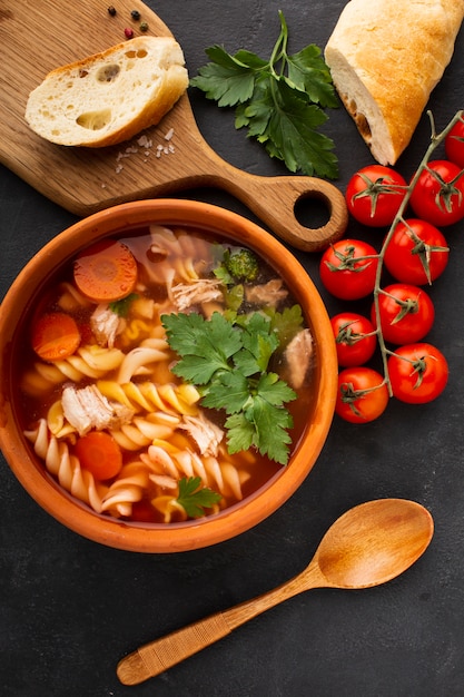 Flat lay broccoli carrots and fusilli in bowl with bread on cutting board and wooden spoon