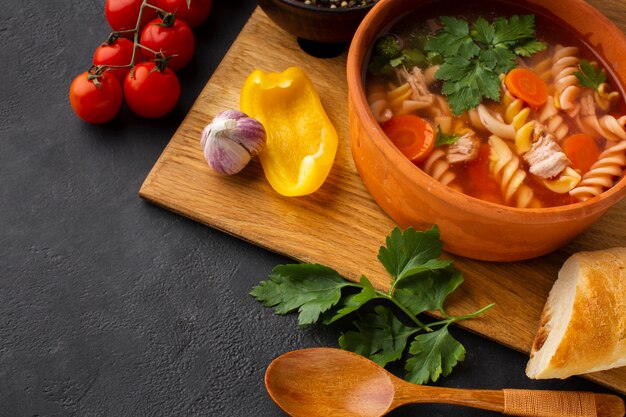 Flat lay broccoli carrots and fusilli soup in bowl with bread and wooden spoon