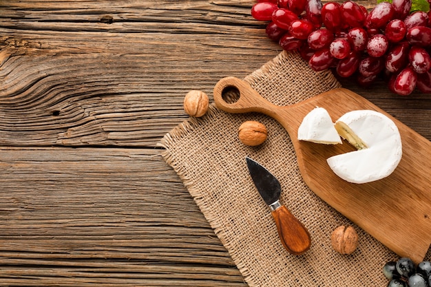 Free photo flat lay camembert grapes and walnuts on wooden cutting board with copy space