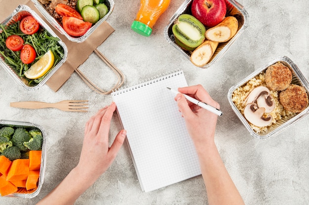 Free photo flat lay of casseroles with meals and hand writing on notebook