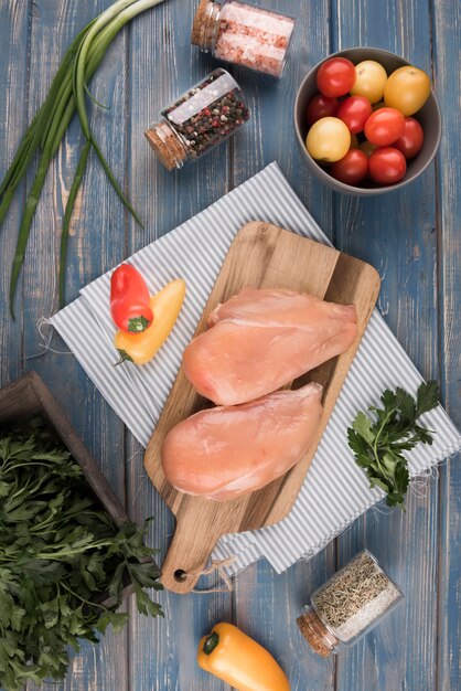 Flat lay chicken breast on wooden board with peppers and tomatoes