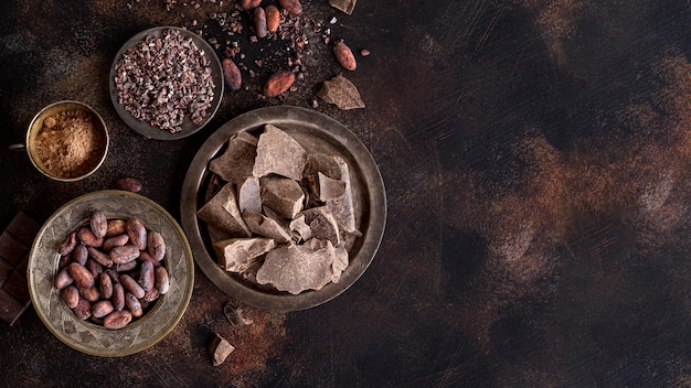 Free photo flat lay of chocolate chunks on plate with cocoa beans and powder and copy space