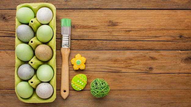 Flat lay of colored easter eggs in carton with paint brush and copy space