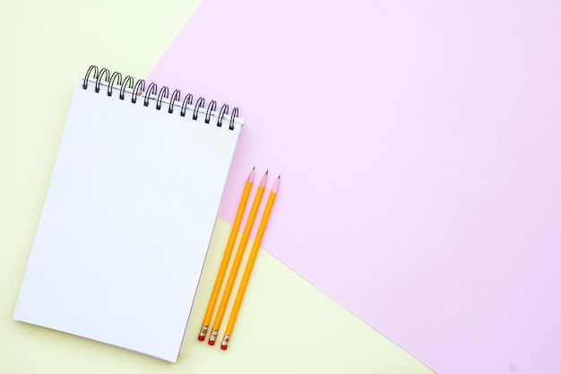 flat lay composition with empty notebook with pencils on pink and yellow background