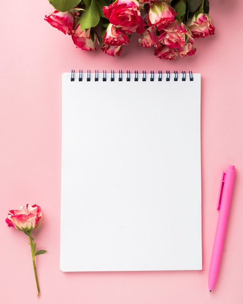 Flat lay of desk with bouquet of roses and notebook