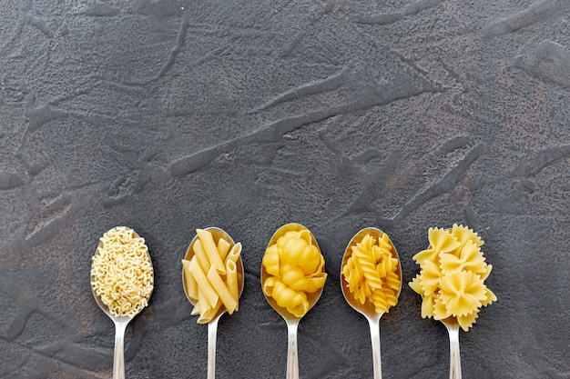 Free photo flat lay of different pasta in spoons with copy space