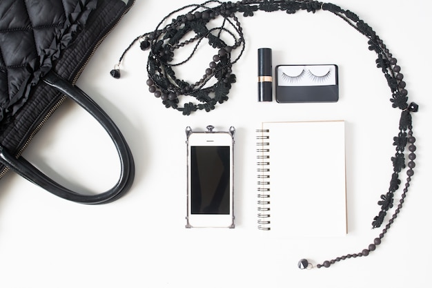 Flat lay of empty notebook, cellphone and woman's accessories in black concept, top view, isolated on white background