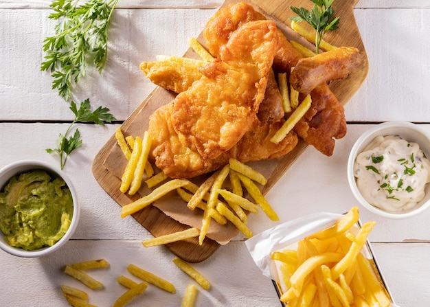 Flat lay of fish and chips on chopping board with sauce