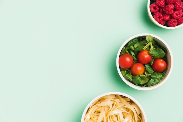 Flat lay food containers with raspberries, salad and pasta with copy-space