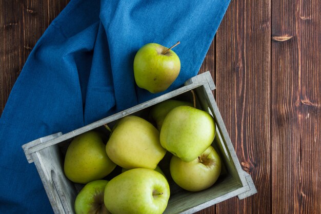 Flat lay green apples in wooden box on blue cloth and wooden background. horizontal