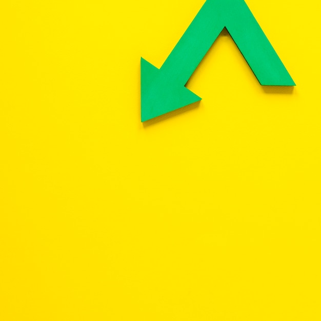 Free photo flat lay green arrow on yellow backgroundwith copy-space