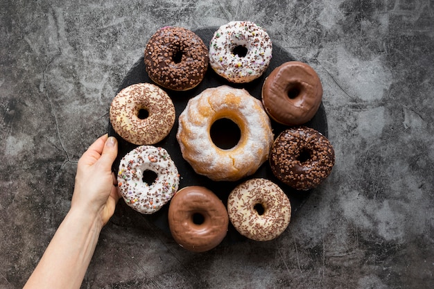 Free Photo flat lay of hand holding plate of doughnuts