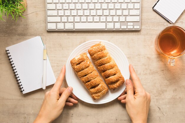 Flat lay hand holding plate of pastry with notebook