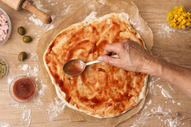 Free photo flat lay hand spreading tomato sauce on pizza dough