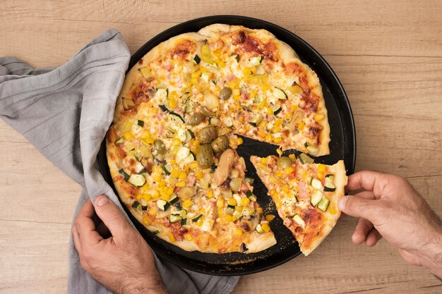 Flat lay hand taking pizza slice from pan with pizza