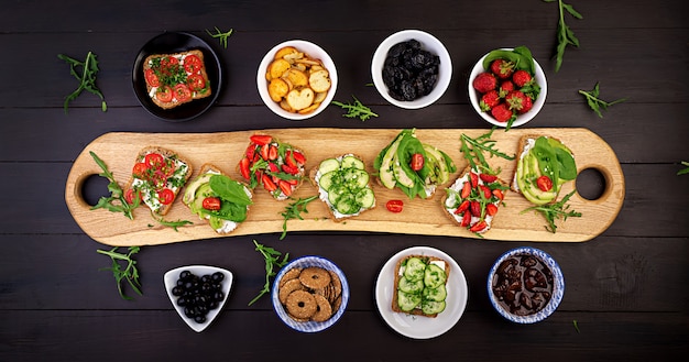 Free photo flat lay of healthy vegetarian dinner table setting. sandwiches with tomato, cucumber, avocado, strawberry, herbs and olives, snacks. clean eating, vegan food