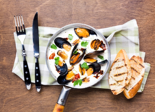 Free photo flat-lay mussels in white sauce with cutlery on tablecloth