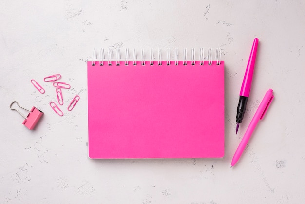 Flat lay of notebook on desk with pen and paper clips