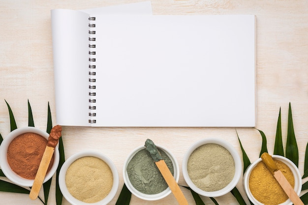 Flat lay of notebook with assortment of bowls with powder