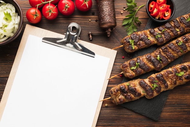 Flat lay of notepad with delicious kebabs and tomatoes