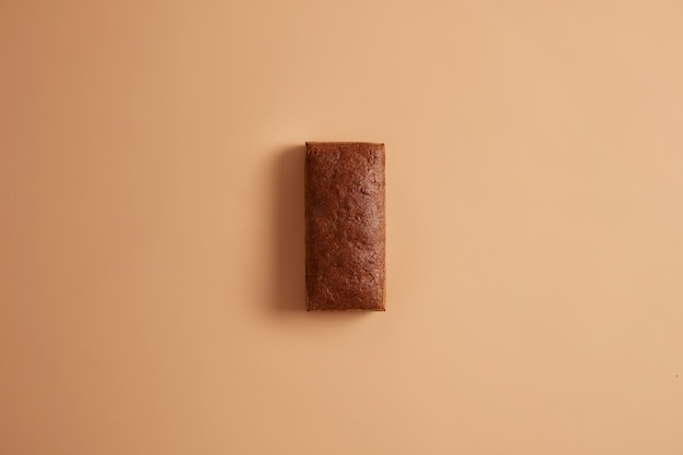 Flat lay of organic dark rye fresh bread in retangular shape prepared from organic flour. Nutrient multigrain product on beige background. Whole loaf ready for consumption. Bakery selection.