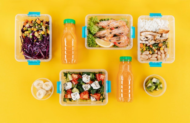 Flat lay of organized plastic food containers with meals and orange juice bottles