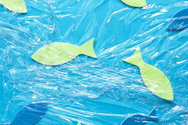 Free photo flat lay of paper fish under plastic wrap