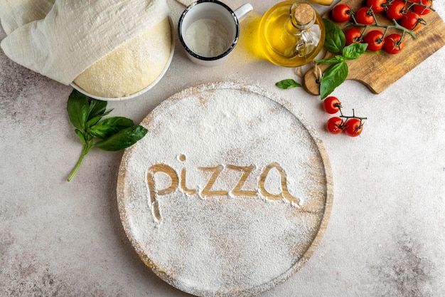 Flat lay of pizza dough with wooden board and word written in flour