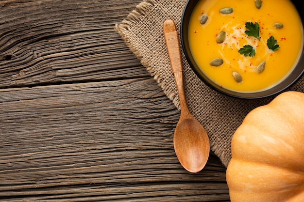 Flat lay pumpkin soup in bowl and wooden spoon with copy space