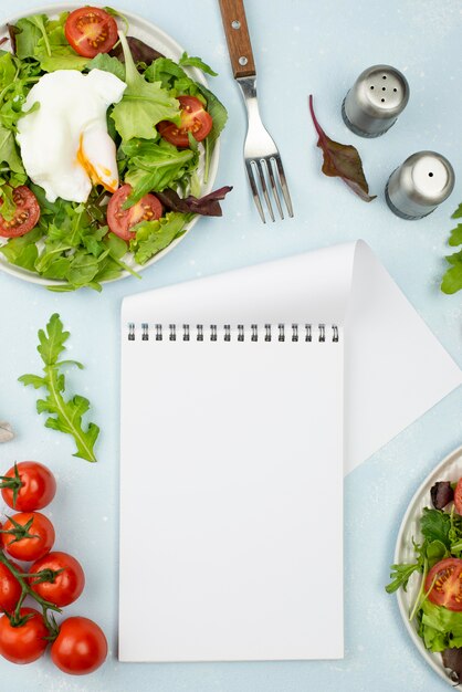 Flat lay salad with fried egg and tomatoes with blank notepad