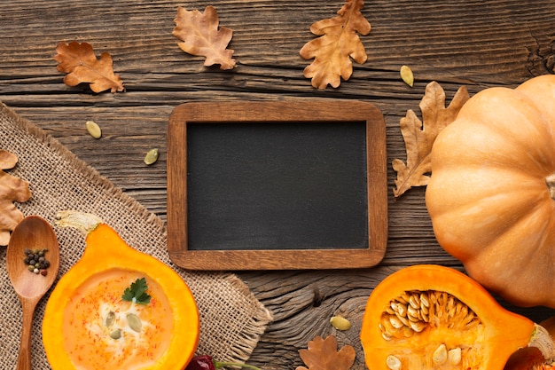 Free photo flat lay sliced pumpkin wooden spoon and leaves with blank blackboard