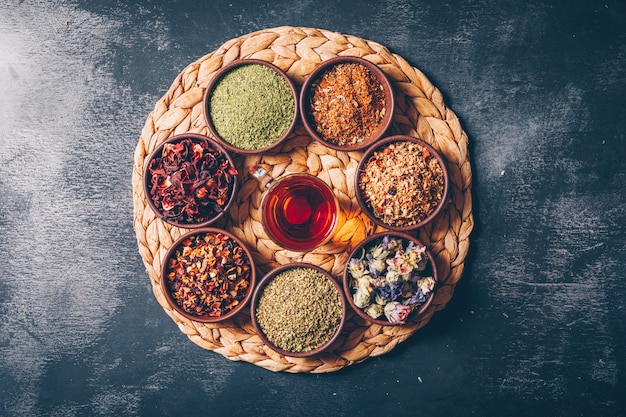 Free photo flat lay tea herbs in bowls with a cup of tea on wooden and dark textured background. horizontal