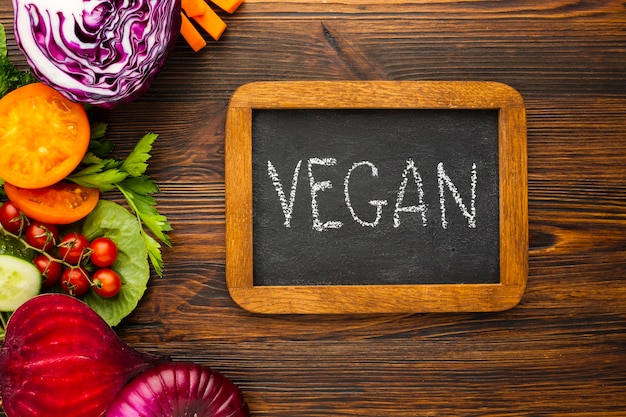 Flat lay vegetable arrangement with vegan lettering on chalkboard 