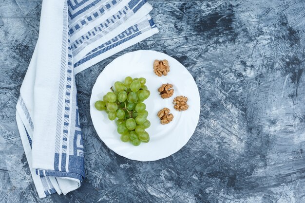 Flat lay white grapes, walnuts in white plate with kitchen towel on dark blue marble background. horizontal