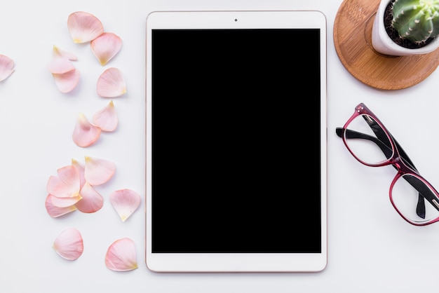 Free photo flat lay with tablet, glasses, cactus and petals on table