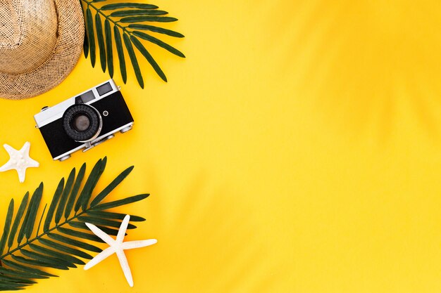 Flat lay with traveler accessories: tropical palm leaf, retro camera, sun hat,  starfish on yellow background