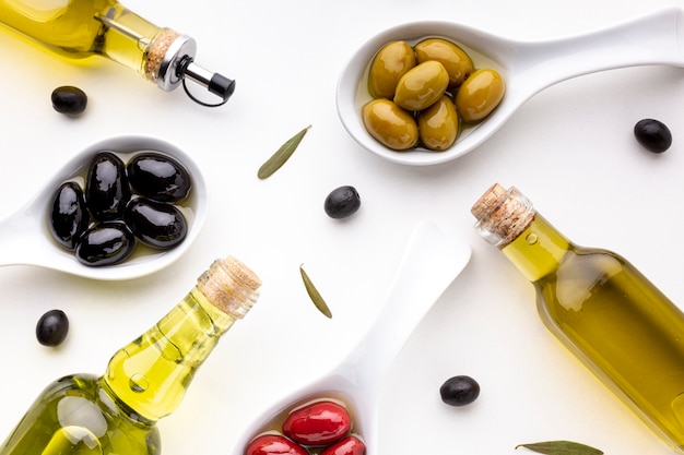 Flat lay yellow red black olives in spoons with oil bottles