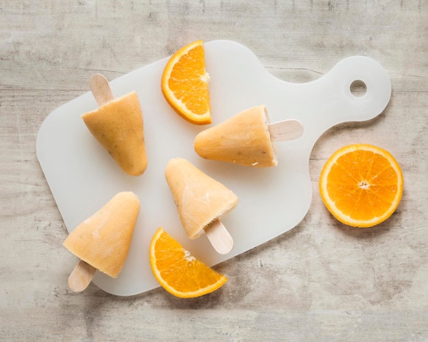 Free photo flat lay of yummy popsicles on chopping board with orange