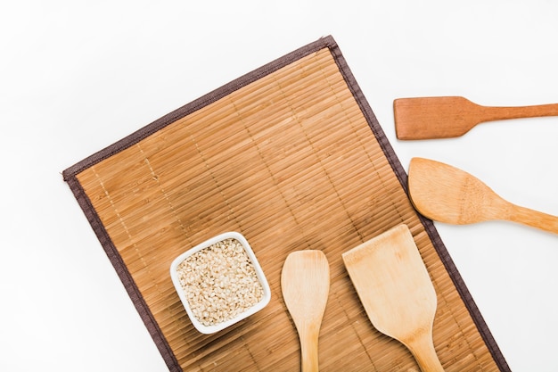 Free Photo flat uncooked rice bowl and wooden spatulas on placemat over white background