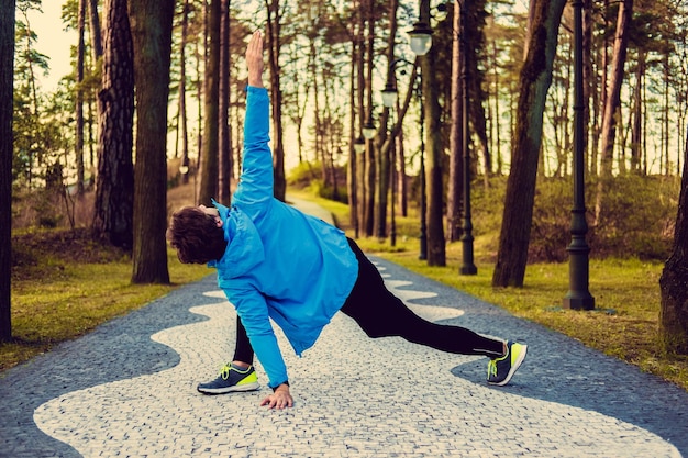 Flexible fitness man in a blue sports jacket exercising outside.