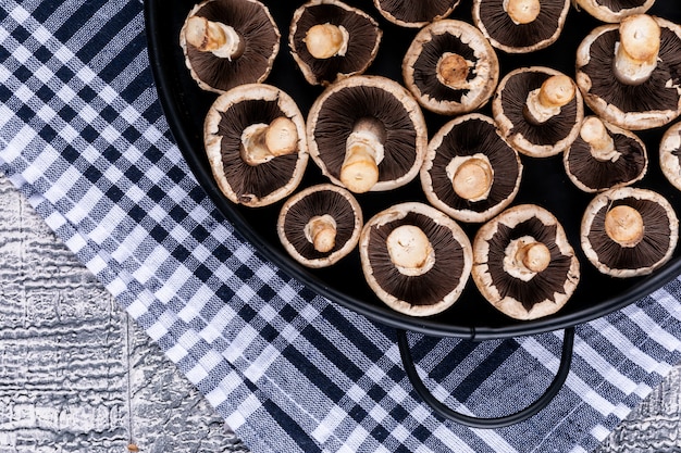 Flipped white mushrooms in a pot on picnic cloth top view on a gray wooden table