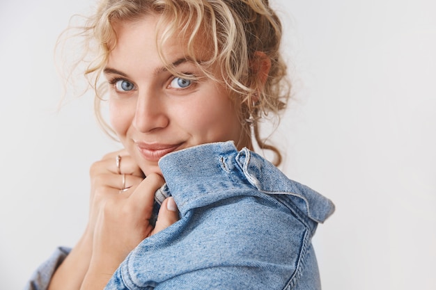 Free photo flirty feminine tender cute romantic girlfriend blond curly hairstyle blue eyed turning camera smirking coquettish look happily enjoying romantic date night-out, standing silly white wall