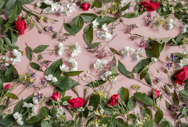 Floral arrangement with different fresh flowers, leaves and twigs on a pink background.