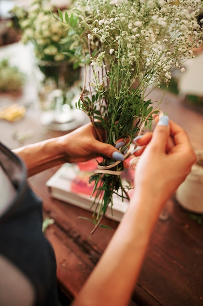 Free photo florist's hand tying bunch of white flowers with string