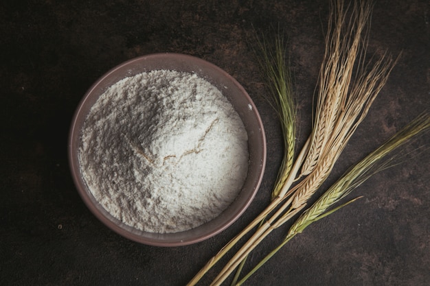 Free photo flour in a bowl with wheat flat lay on a dark brown