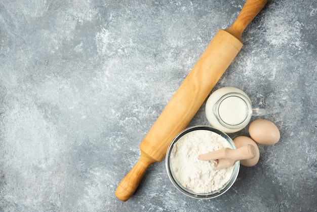 Flour, eggs, milk and rolling pin on marble.