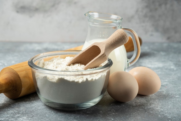 Flour, eggs, milk and rolling pin on marble.